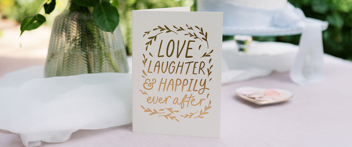 Martha Brook Personalised Happy Ever After Embossed Wedding Card on a pink table with a vase
