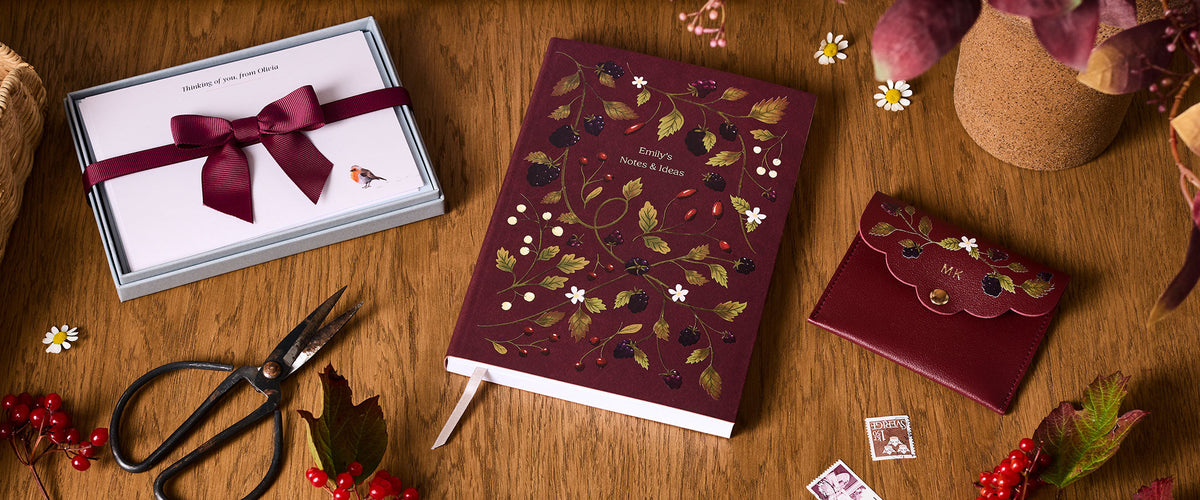 Martha Brook Personalised Berries and Brambles Notebook on a desk with Berries and Brambles Mini Pouch and Robin Notecards