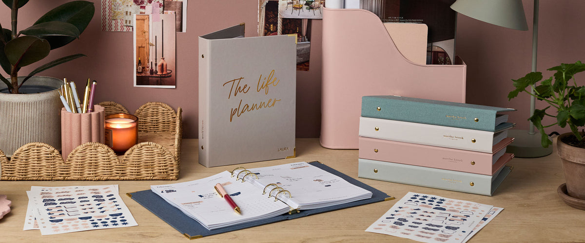 Martha Brook Life Planner open on a desk next to a stack of Life Planners and stickers