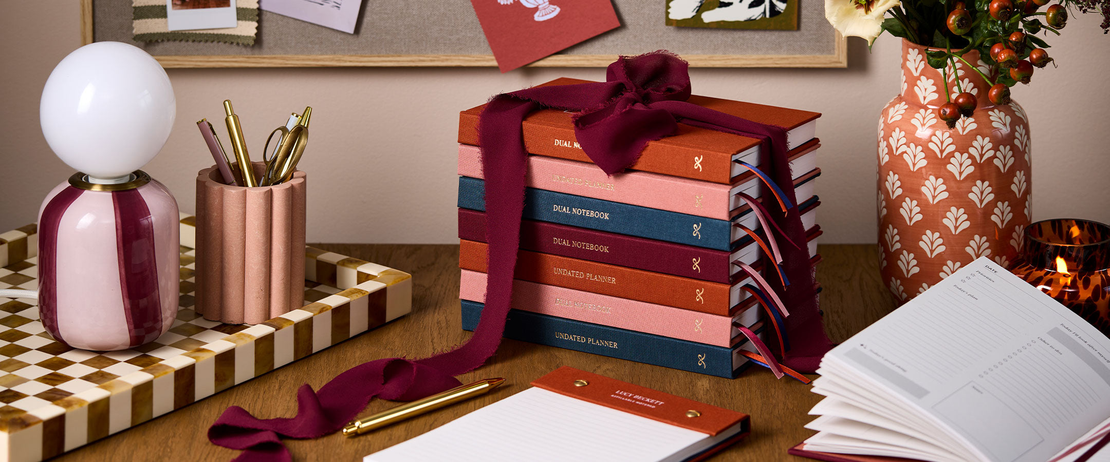 Martha Brook signature collection notebooks stacked on a brown table with a pink pen pot