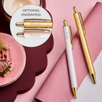 martha brook gold ballpoint pen white and gold pen next to gold pen both with an engraved name on a vegan leather pink notebook. There is a circle highlighting the engraved name example.