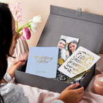 martha brook personalised luxury engagement gift box on a table covered in pink linen. The box is opened to reveal a wedding notes notebook, a gold photo holder and an engagement card that reads love laughter and happily ever after