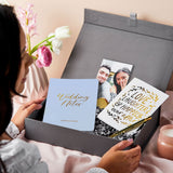 martha brook personalised luxury engagement gift box on a table covered in pink linen. The box is opened to reveal a wedding notes notebook, a gold photo holder and an engagement card that reads love laughter and happily ever after