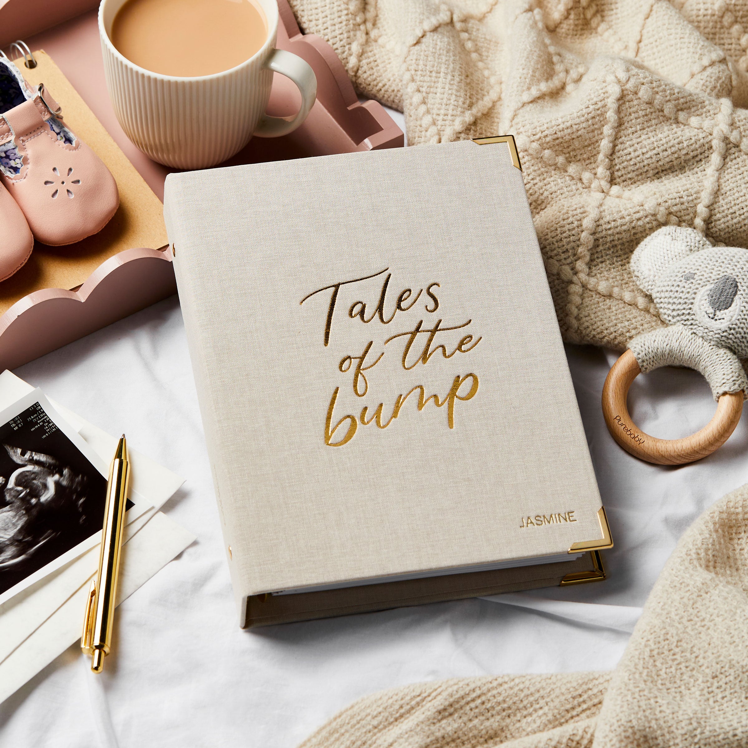 Martha Brook Pregnancy Journal and Organiser on a bed with baby shoes and a baby teether