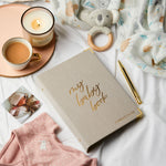 martha brook personalised baby journal and organiser on bed spread with candle and baby grow and baby rattle wide