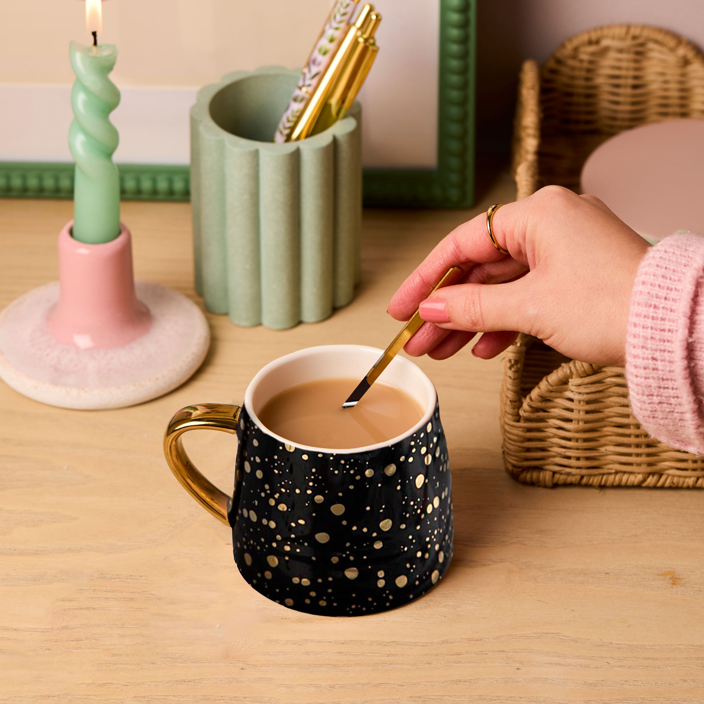 martha brook personalised stationery gold speckled black mug on a wooden desk with spiral green candle and rattan scalloped tray