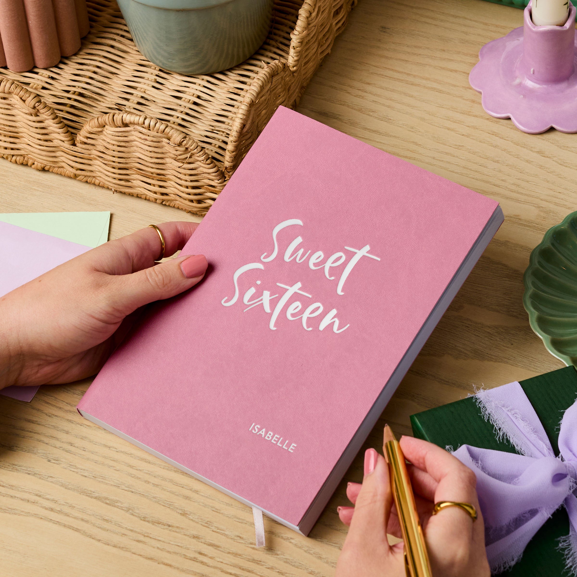 martha brook personalised stationery personalised 16th birthday gift notebook main image pink vegan leather notebook on a wooden desk. The cover of the notebook reads 'sweet sixteen' in silver foil