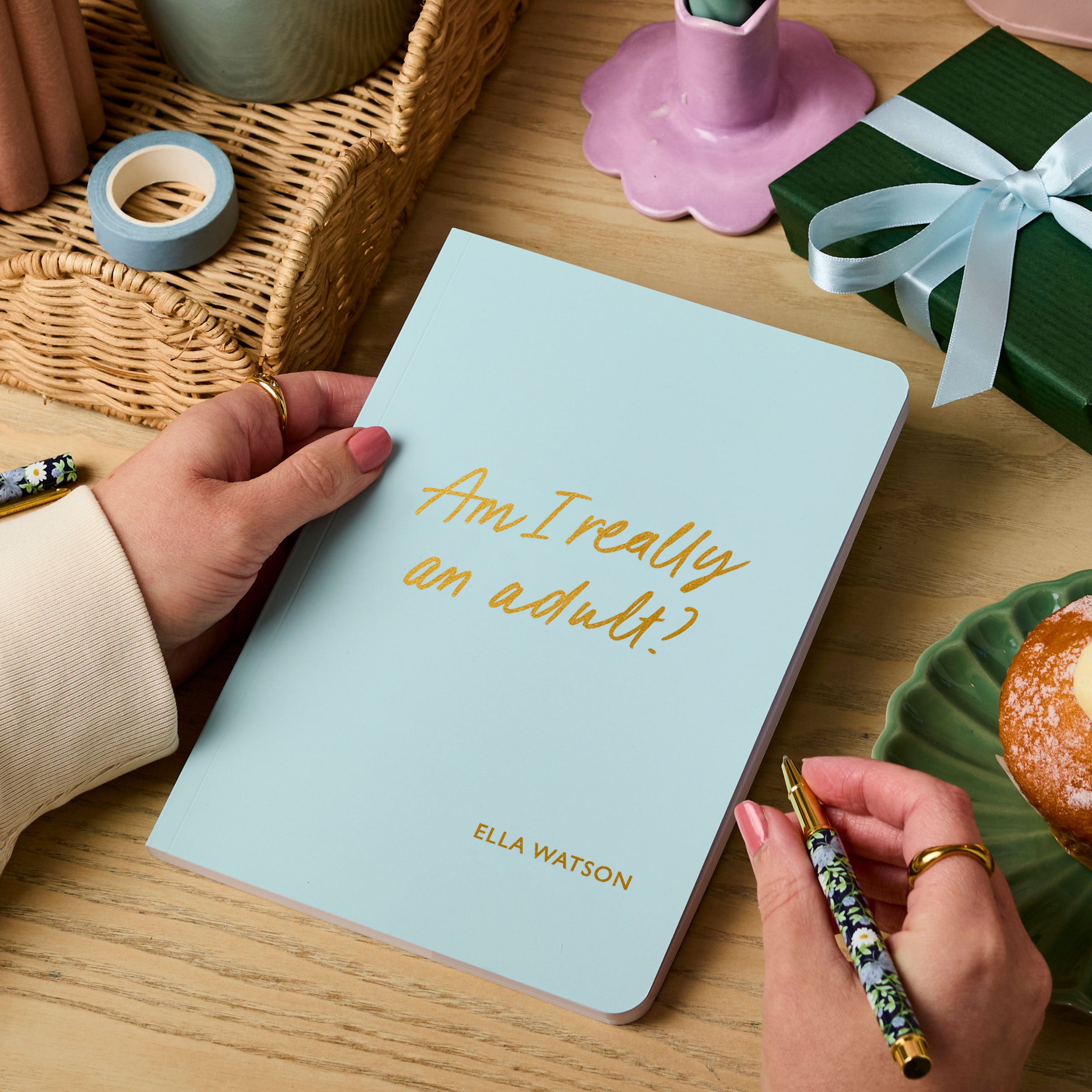 Martha Brook personalised stationery personalised 18th birthday gift softback notebook main image. A pale blue notebook on a wooden desk. The notebook reads 'Am I really an adult? in gold foiling