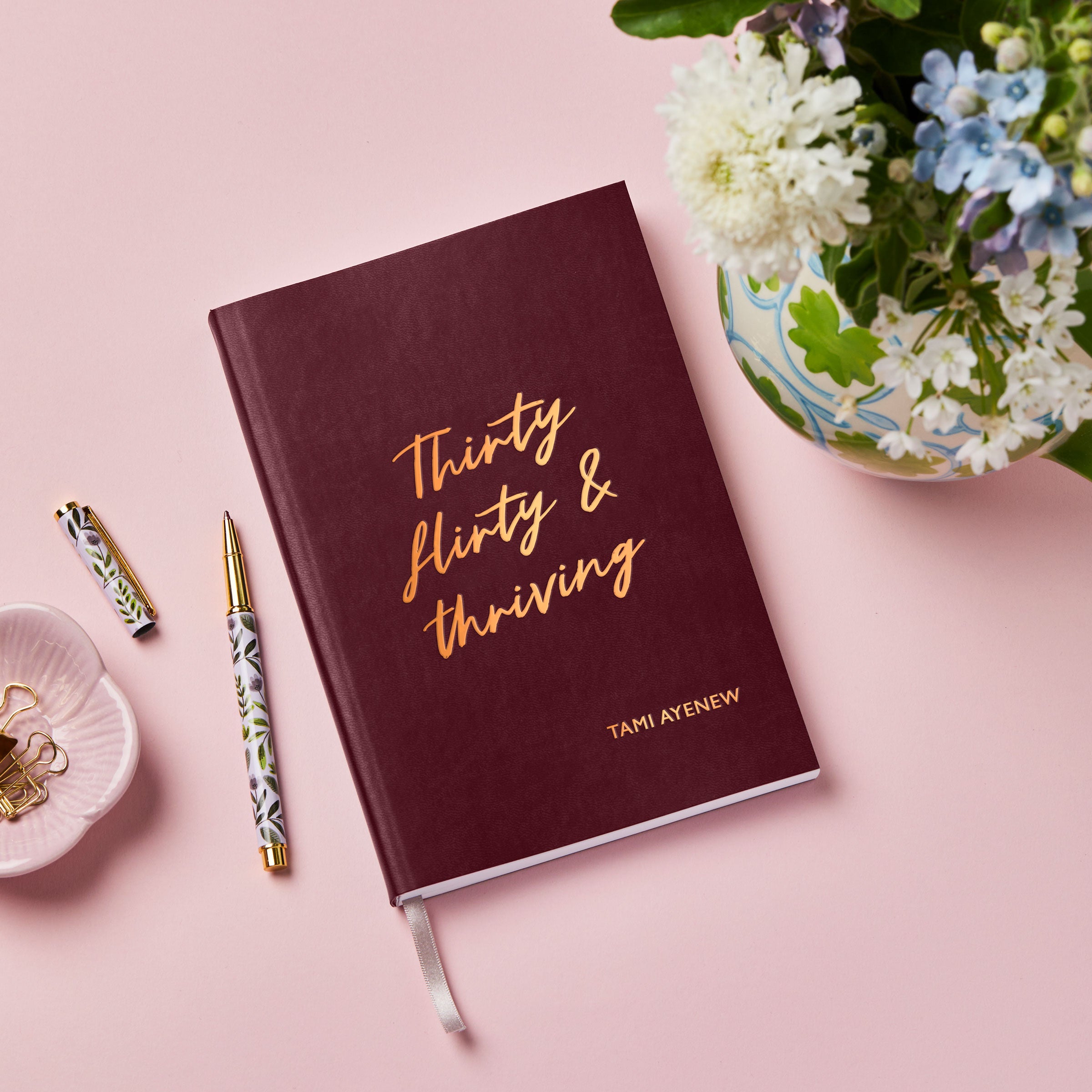 martha brook personalised stationery personalised 30th birthday gift notebook. A red vegan leather notebook on a pink background reads 'thirty, flirty and thriving' on the cover in gold foil