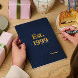 Martha Brook personalised stationery personalised any year birthday softback notebook navy blue notebook on desk with 'est. 1999' embossed on the cover in gold foil