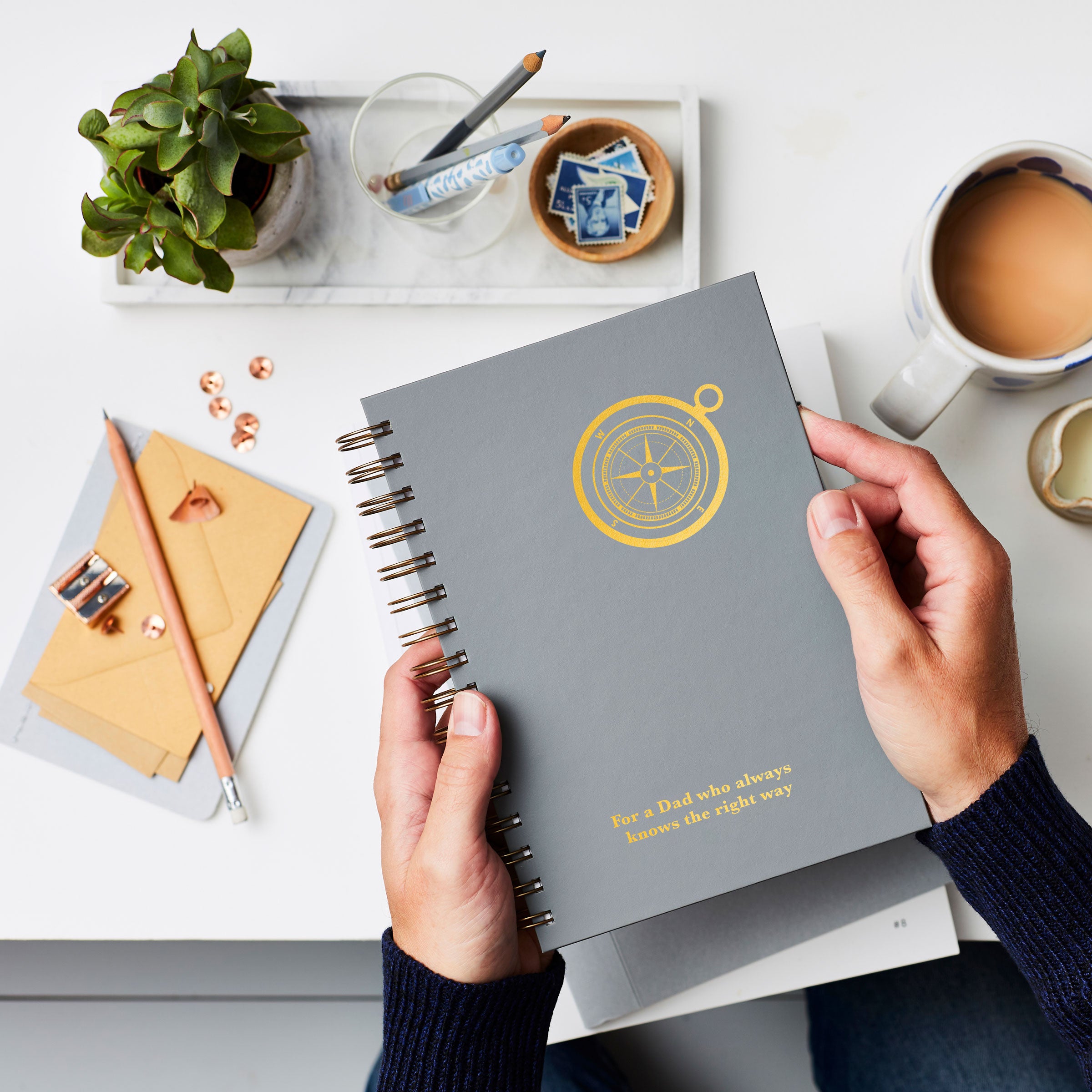 martha brook personalised stationery personalised compass luxe hardback notebook in slat grey with gold foil on a coffee table with a mug of tea and marble tray