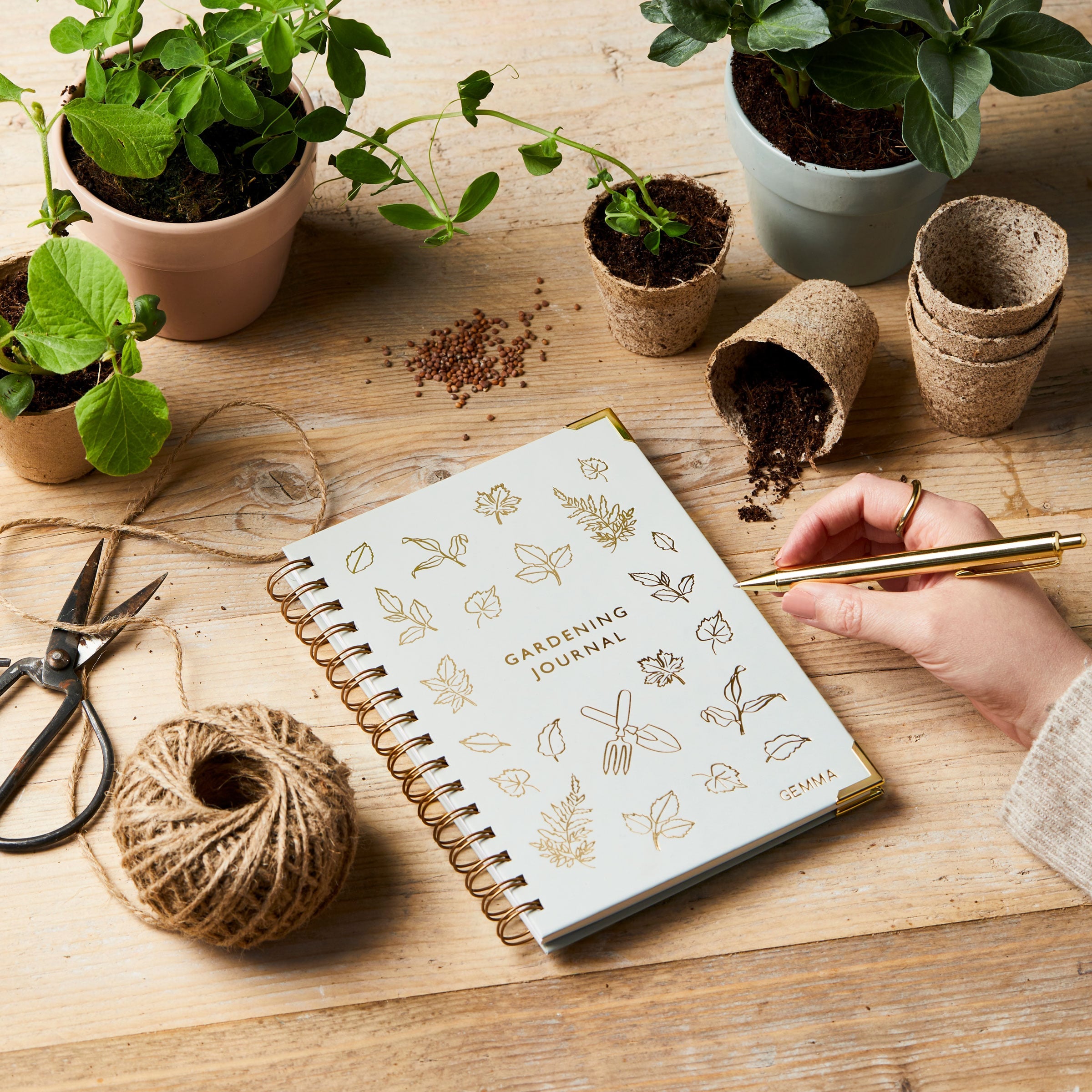 martha brook personalised stationery personalised hardback gardening journal on gardening table with pots and seeds with a hand