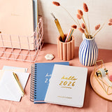 martha brook personalised hello 2026 weekly diary on a pink desk with blue striped dried flower vase and pastel scalloped pen pot
