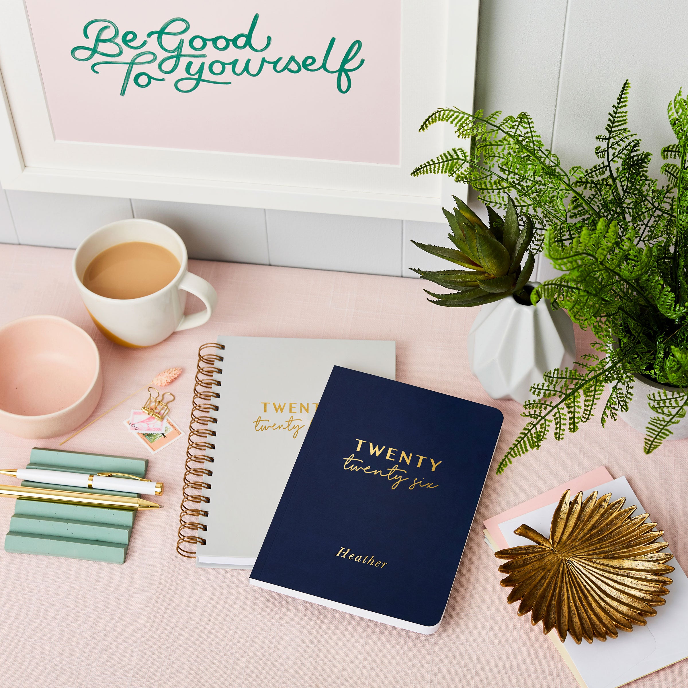 martha brook personalised stationery personalised brilliant 2026 weekly diary navy diary stacked on top of pebble grey hardback diary on a pink desk with cup of tea
