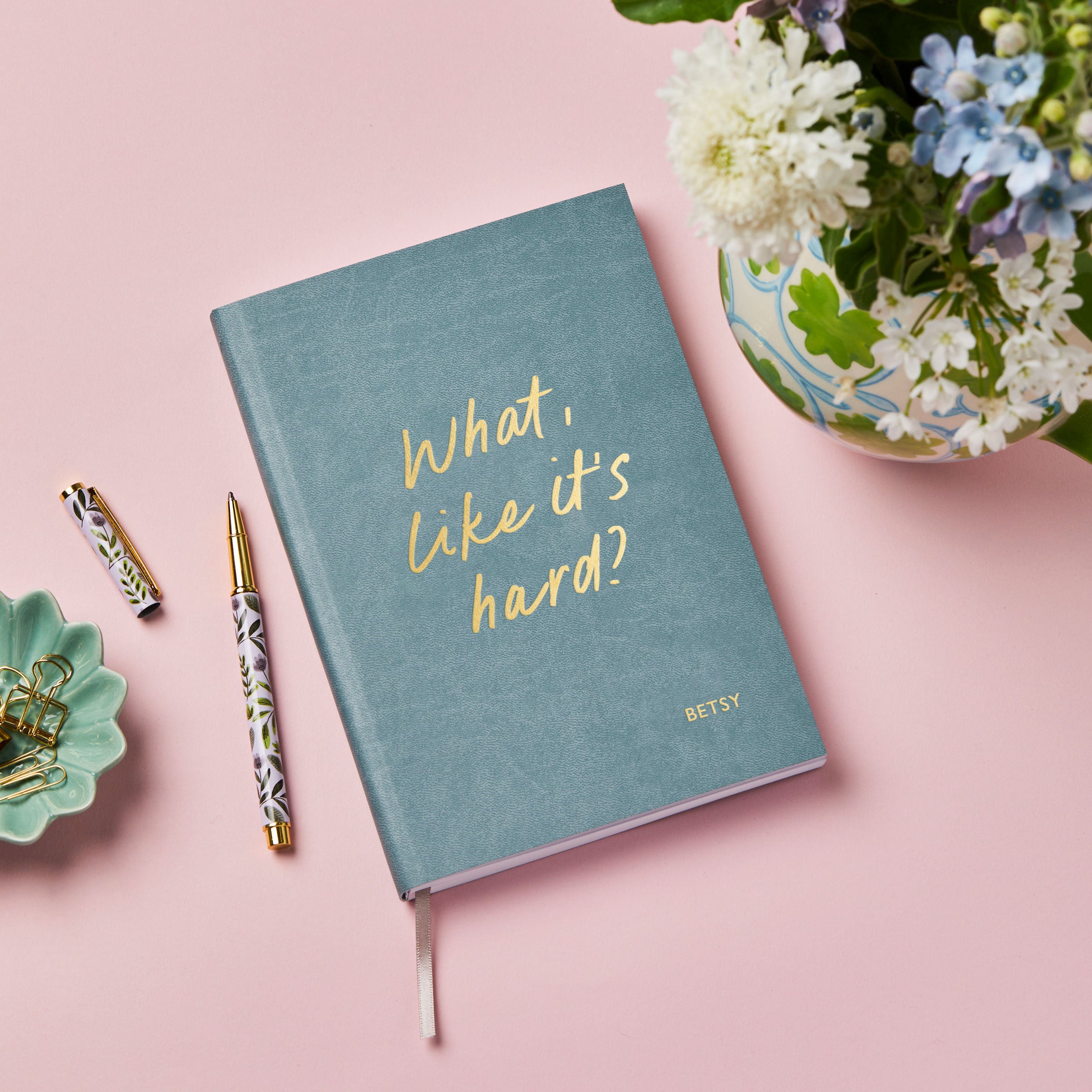 martha brook personalised stationery personalised university gift softback notebook blue vegan leather notebook on a pink background. The notebook reads 'what, like it's hard?' on the cover in gold foil
