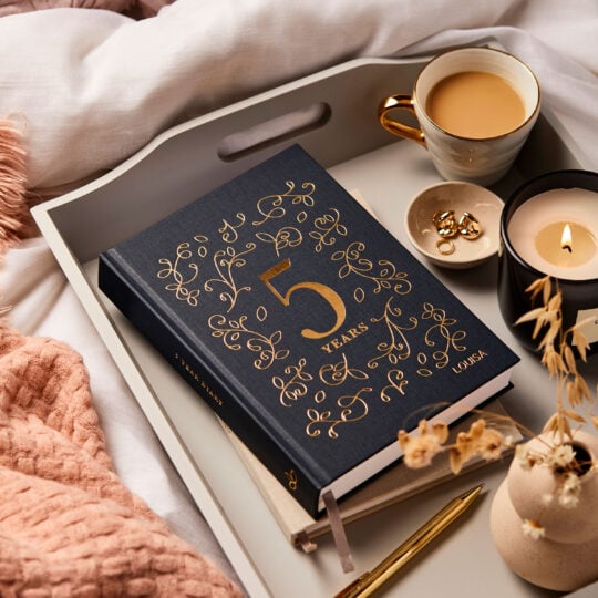 martha brook personalised stationery personalised five year diary in navy and gold foiling on bed spread and tea and candles and blankets