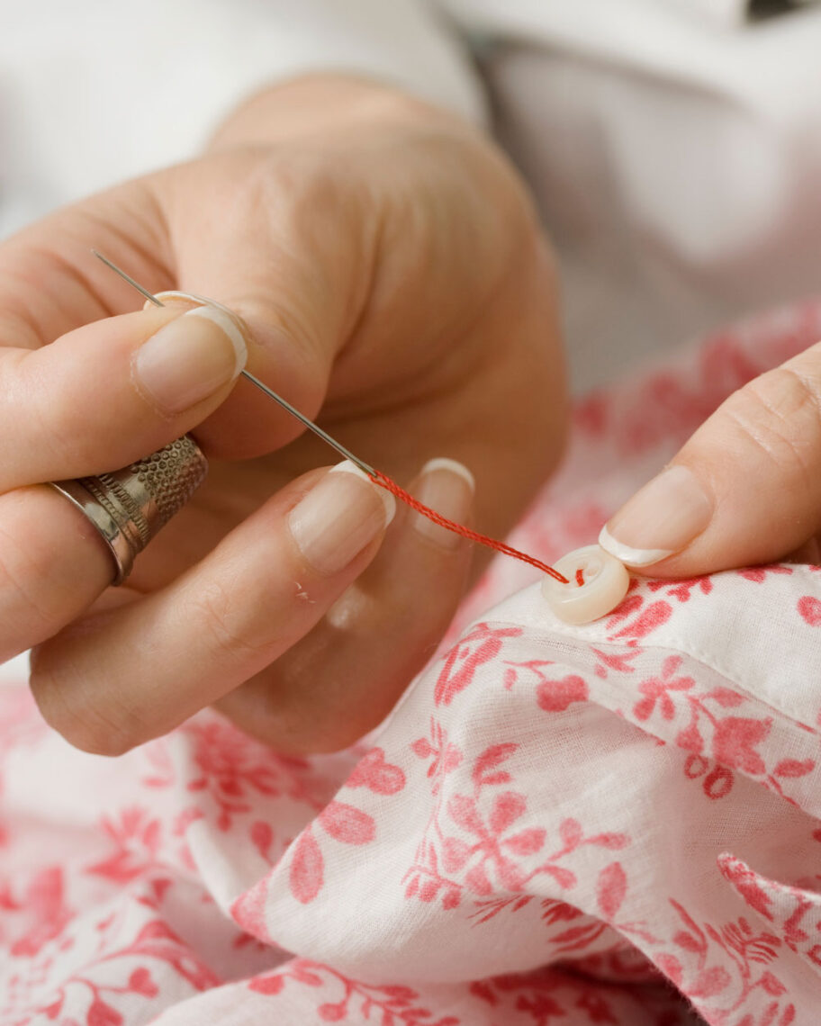 martha brook personalised stationery blog 15 things to take on holiday that you’ll wish you’d thought of sooner sewing kit. Person sewing a button back onto a white and pink flowery top using red thread