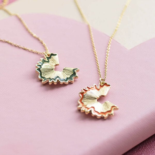 Martha Brook personalised stationery blog 10 wonderful gift ideas for teachers to say thank you joy by corrine smith pencil shaving necklace in gold. Two gold necklaces are laying on a pink table, The necklaces both have a pendant in the shape of a pencil shaving, one in orange and one in green.