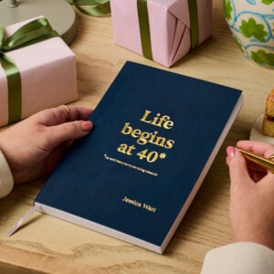 martha brook personalised stationery personalised 40th birthday gift notebook navy blue notebook on a wooden desk. The notebook reads 'life beings at 40. Up until then you're just doing research' in gold foil on the cover