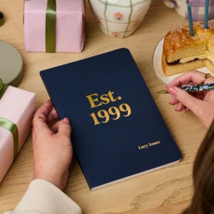 Martha Brook personalised stationery personalised any year birthday softback notebook navy blue notebook on desk with 'est. 1999' embossed on the cover in gold foil