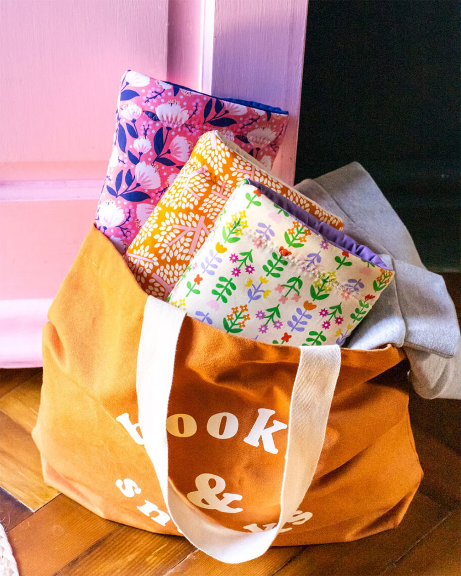 Martha Brook personalised stationery blog 10 dreamy school supplies for grown-ups that give us that back to school feeling paper and wood book sleeve. An orange tote bag on the floor with three colourful patterned fabric book sleeves poking out of the top 