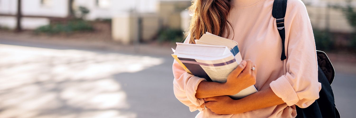Martha Brook personalised stationery blog Our university essentials and top tips if you’re heading off to study this year woman in a pink jumper holding a stack of books