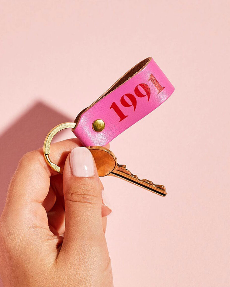 martha brook personalised stationery blog 10 unique birth year personalised birthday gifts create gift love personalised keyring. A pink background, in front of it a hand holding a key. The key has a bright pink leather loop keyring with '1991' written on it in red text.