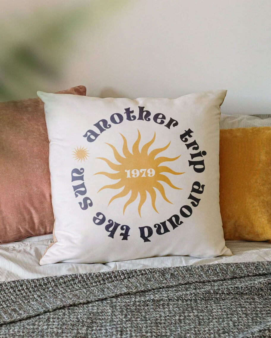 martha brook personalised stationery blog 10 unique birth year personalised birthday gifts drifting bear co personalised birthday cushion. A cream coloured cushion on a sofa, embellished with the text 'another trip around the sun' in a cricle. In the middle of the circle is a yellow sun, with the year '1979' in white text.