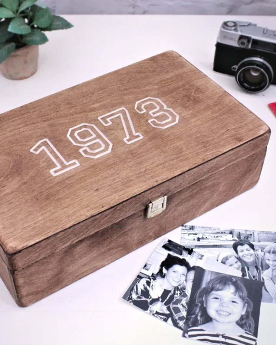 martha brook personalised stationery blog 10 unique birth year personalised birthday gifts warners end personalised memory box. A wooden keepsake memory box on a table with a pile of black and white family photographs in front. The top of the box reads '1973' in white text.