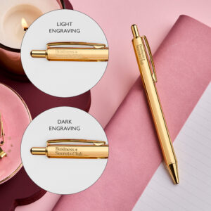 Branded gold pen with symbol engraved on it, on a pink notebook background. Two bubbles, one showing light engraving and one showing dark engraving